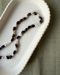 Dark red garnet nugget beads and small baroque pearls strung on a wine coloured silk, draped in a white scalloped dish on an olive background